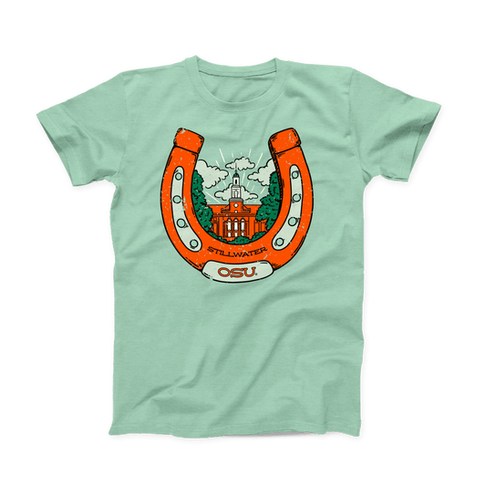 Mint green colored OSU T-shirt. Screen printed in orange is a large, upright horseshoe with "Stillwater" in small black font at the bottom, with "OSU" a little larger below that on the horseshoe. Inside the horseshoe is the Edmon Low Library building surrounded by green trees and white clouds.  